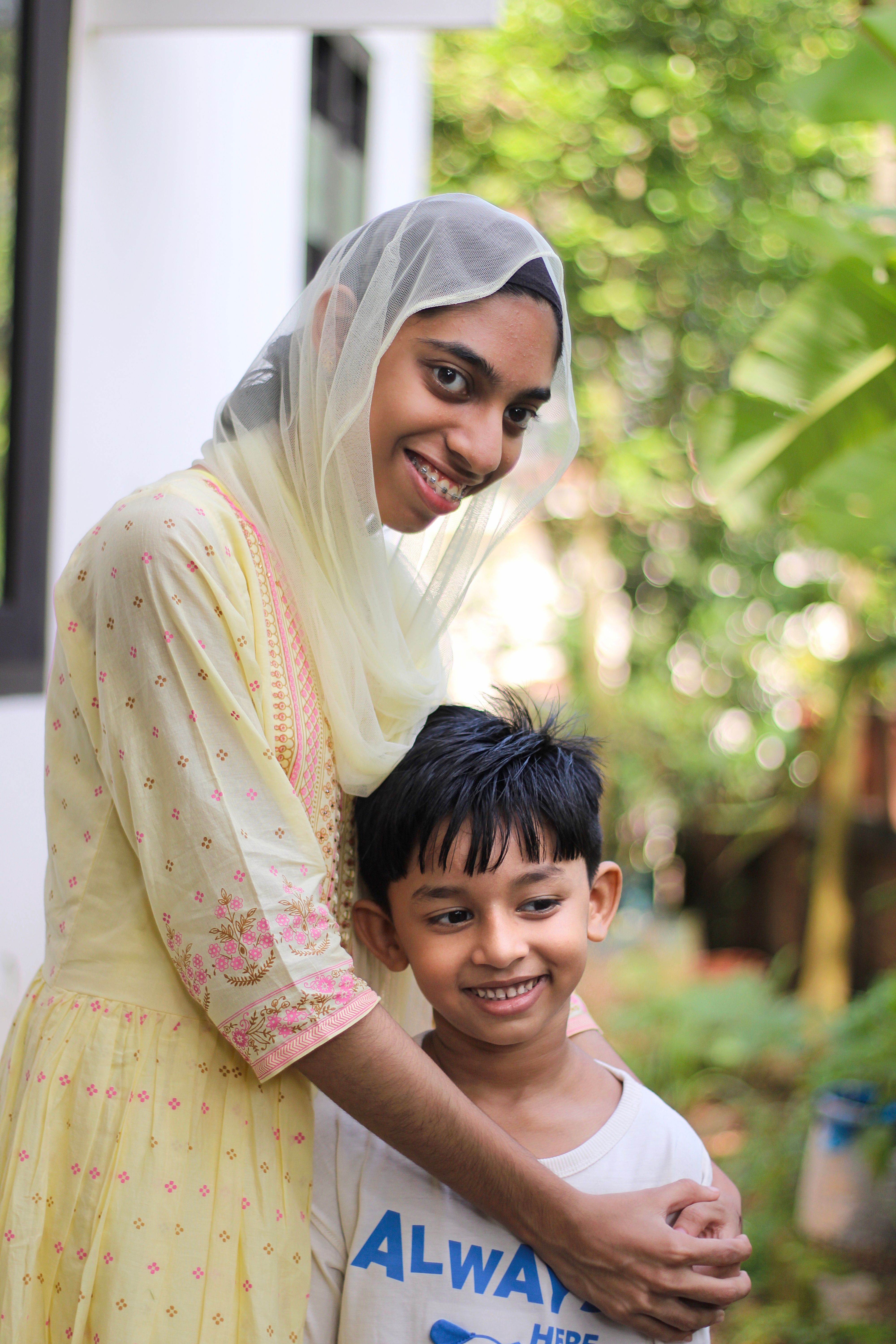Portrait of a smiling woman in a headscarf embracing a young boy outdoors.