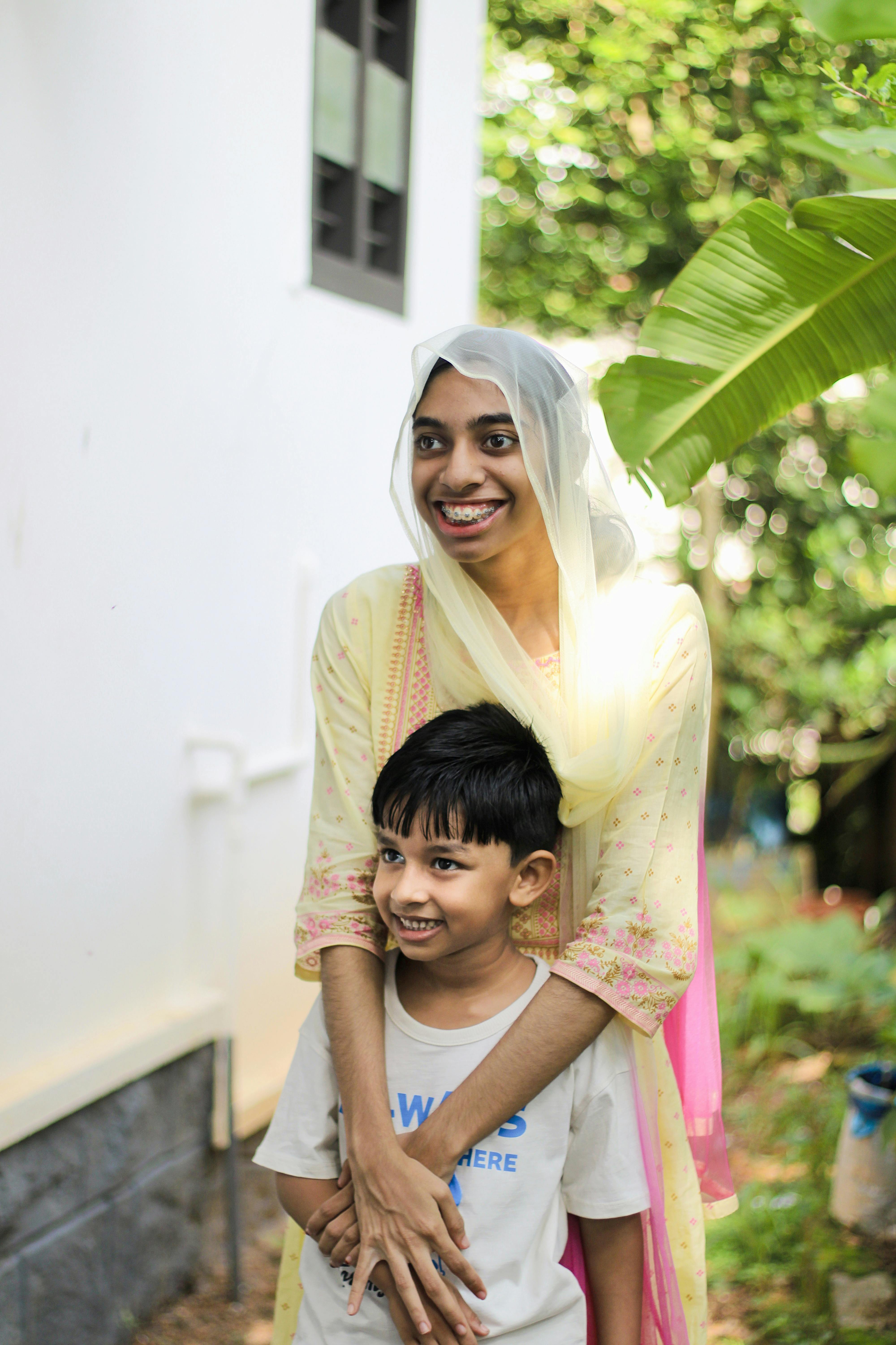A cheerful mother in a headscarf embraces her son in a lush garden setting, exuding warmth and happiness.