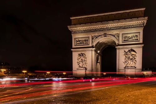 Free Long exposure capturing light trails around the iconic Arc de Triomphe at night in Paris, France. Stock Photo