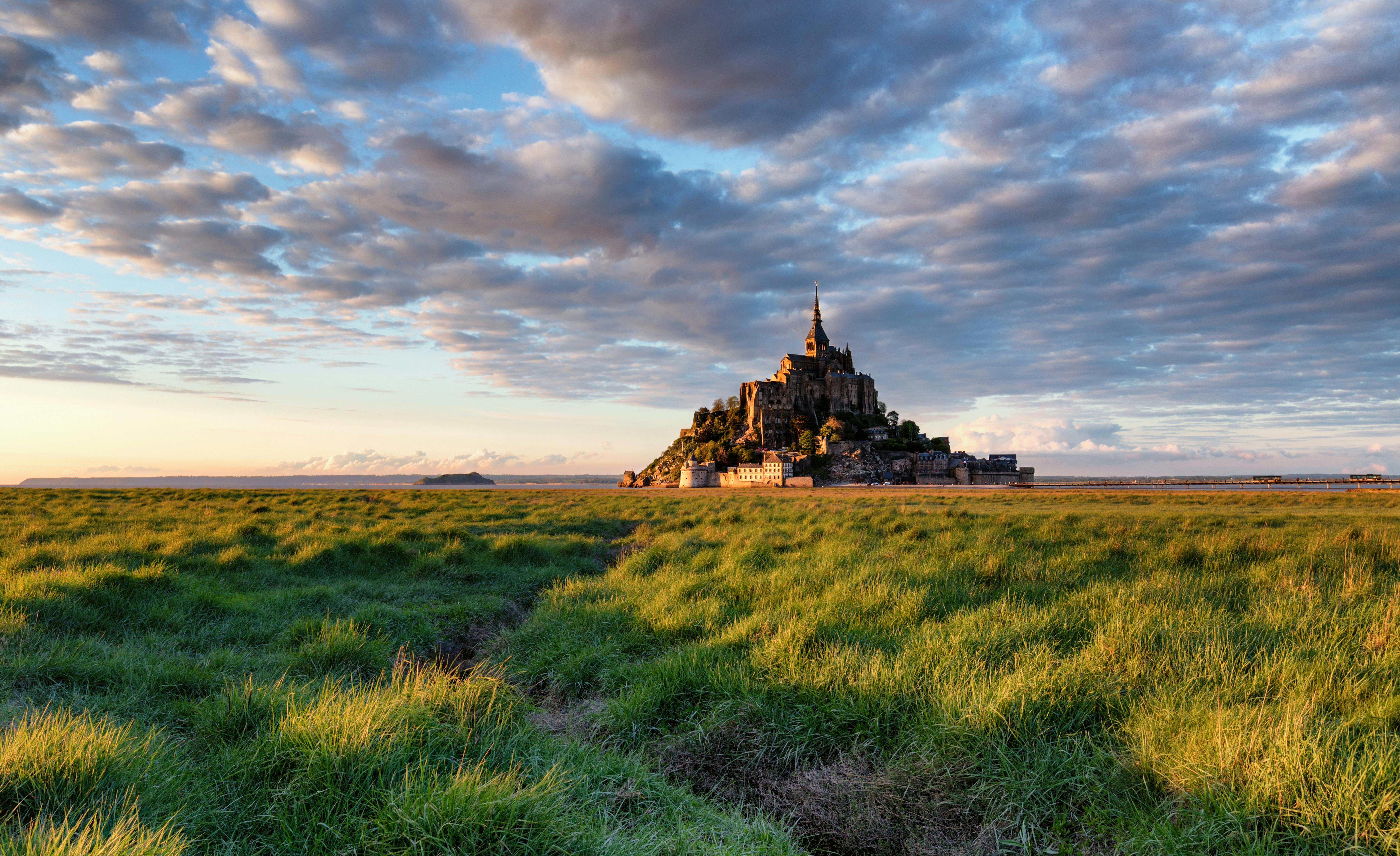 Capture of Mont Saint-Michel in Normandy during sunset over lush green fields.
