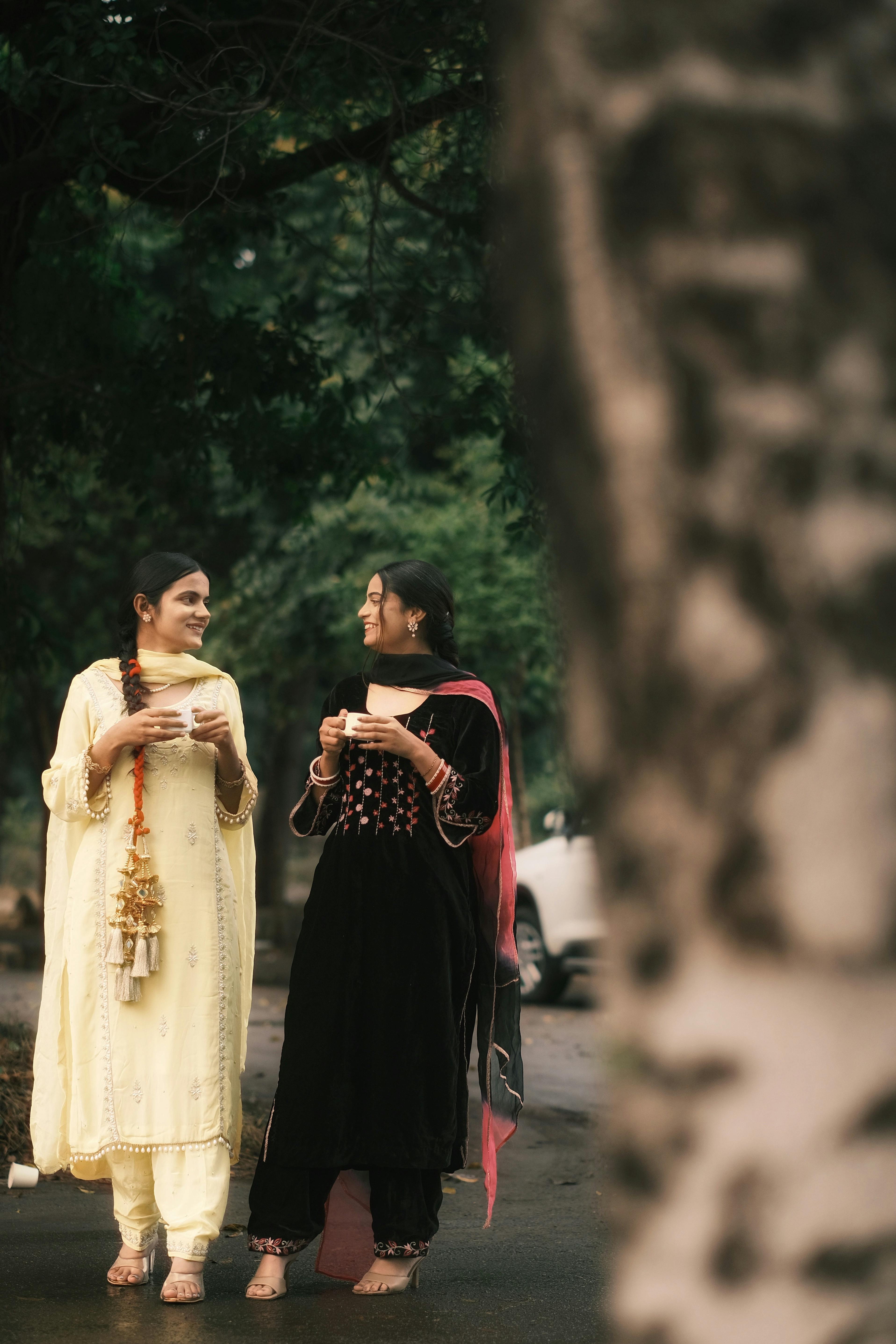 Two women in traditional Punjabi attire enjoying a casual outdoor stroll while holding cups.
