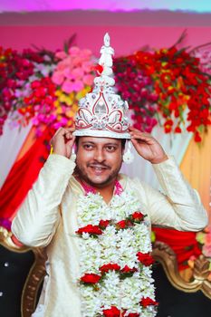 A joyous South Asian groom wearing vibrant traditional attire, adorned with floral and cultural elements.