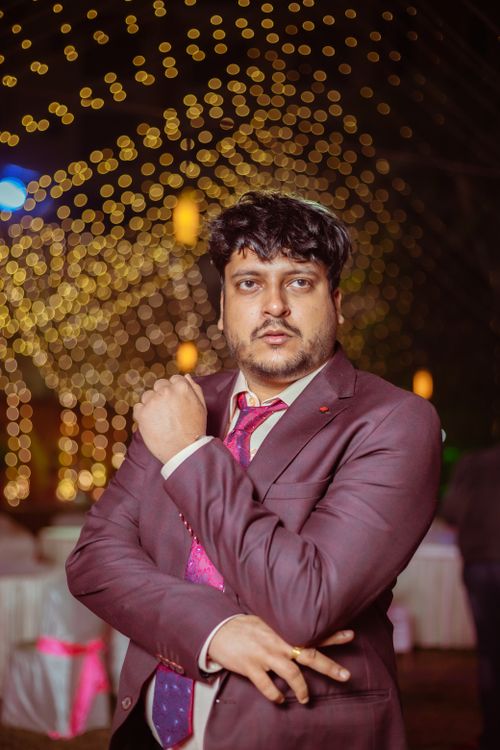 Free Man in a maroon suit posing at a festive event with bokeh lights background. Stock Photo