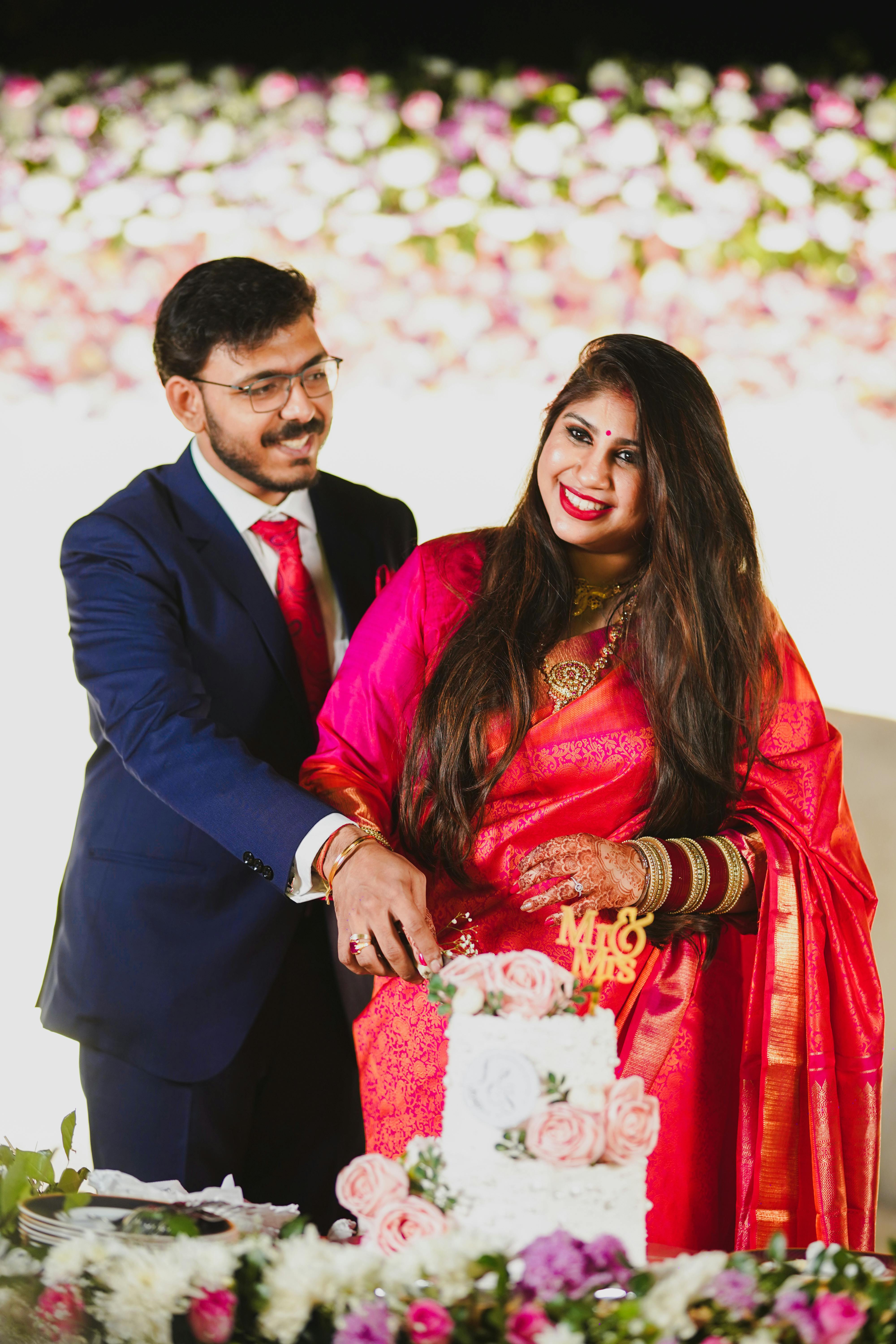 Happy couple in traditional Indian attire cutting wedding cake during a vibrant ceremony.