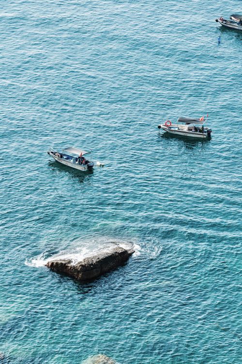 Free Two small boats traverse clear turquoise waters near a rocky outcrop, creating a serene seascape view. Stock Photo