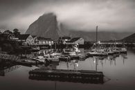Black and white harbor scene in Nordland, Norway with boats, houses, and misty mountains.