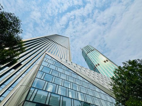 A low-angle view of modern skyscrapers with glass facades under a cloudy blue sky.