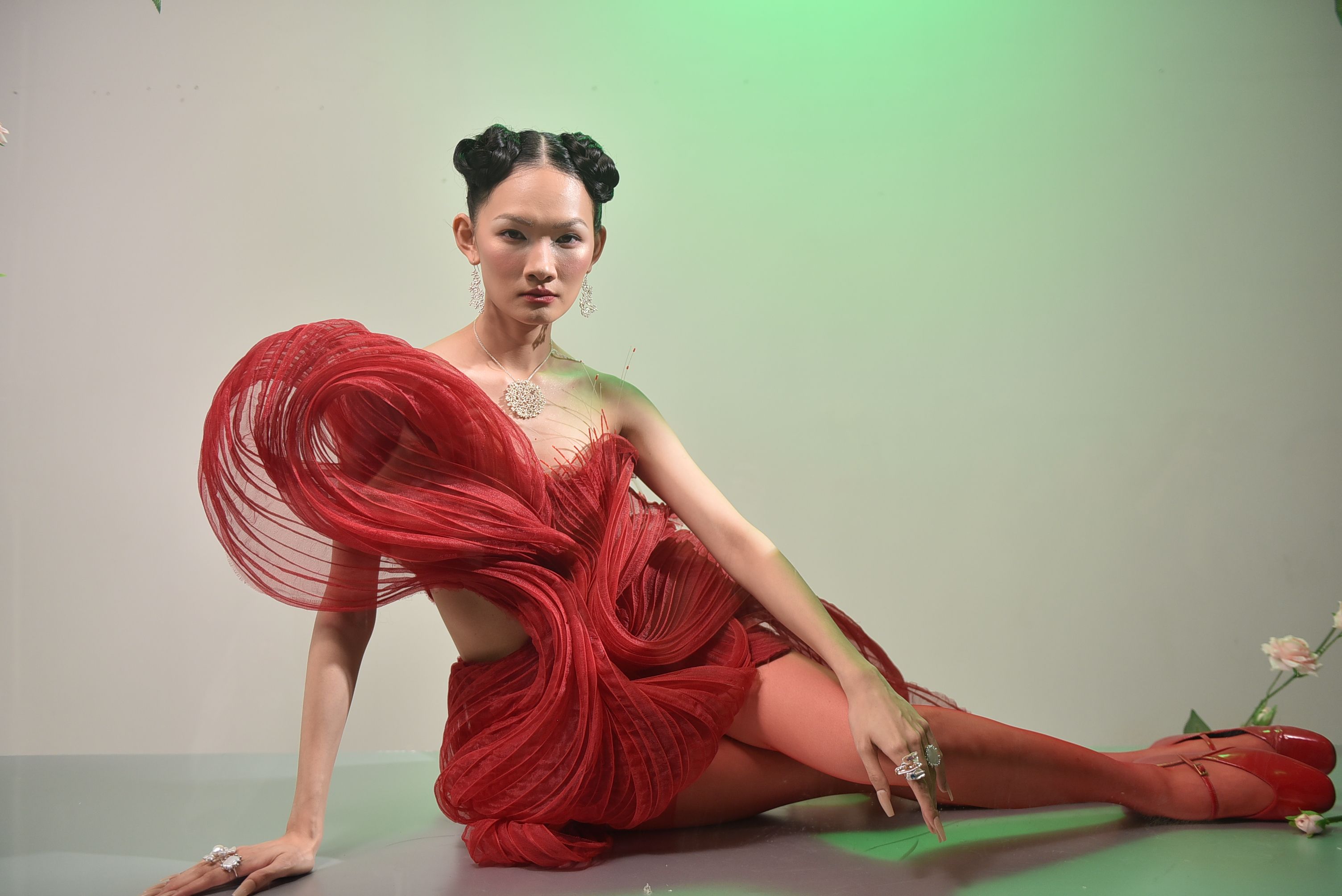 A striking fashion photograph of a model in a red gown with artistic flair, posing elegantly indoors.