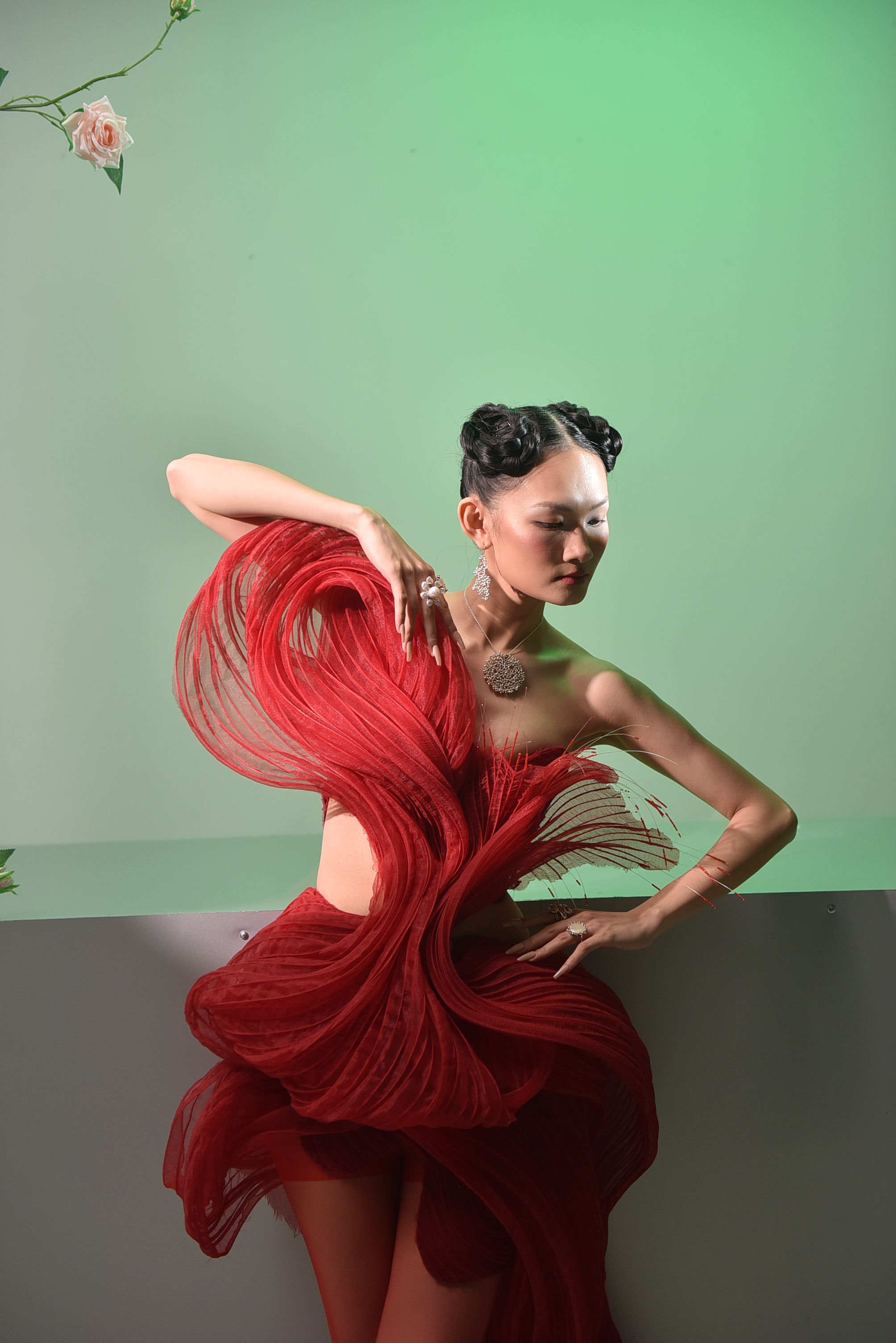 Fashion model posing in a dramatic red dress with a green background, showcasing artistic elegance.