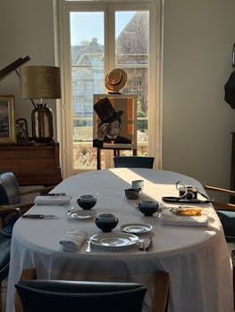 Sunlit dining room with elegant table setting, art piece, and modern interior design elements.