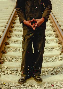An individual in dark clothing stands on railway tracks, adorned with colorful confetti.