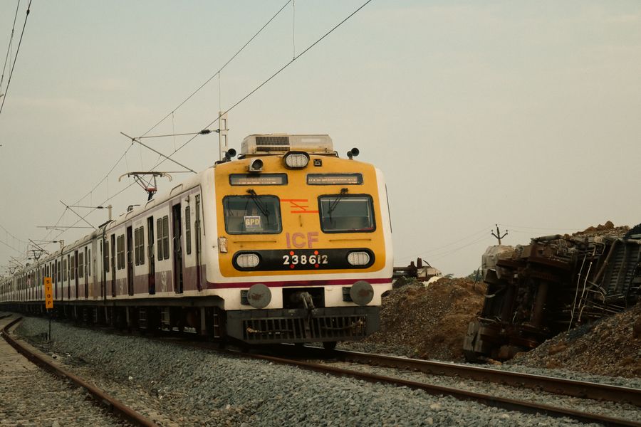 A suburban train traveling on tracks next to a derailed train on a cloudy day.