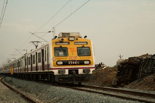 Free A suburban train traveling on tracks next to a derailed train on a cloudy day. Stock Photo