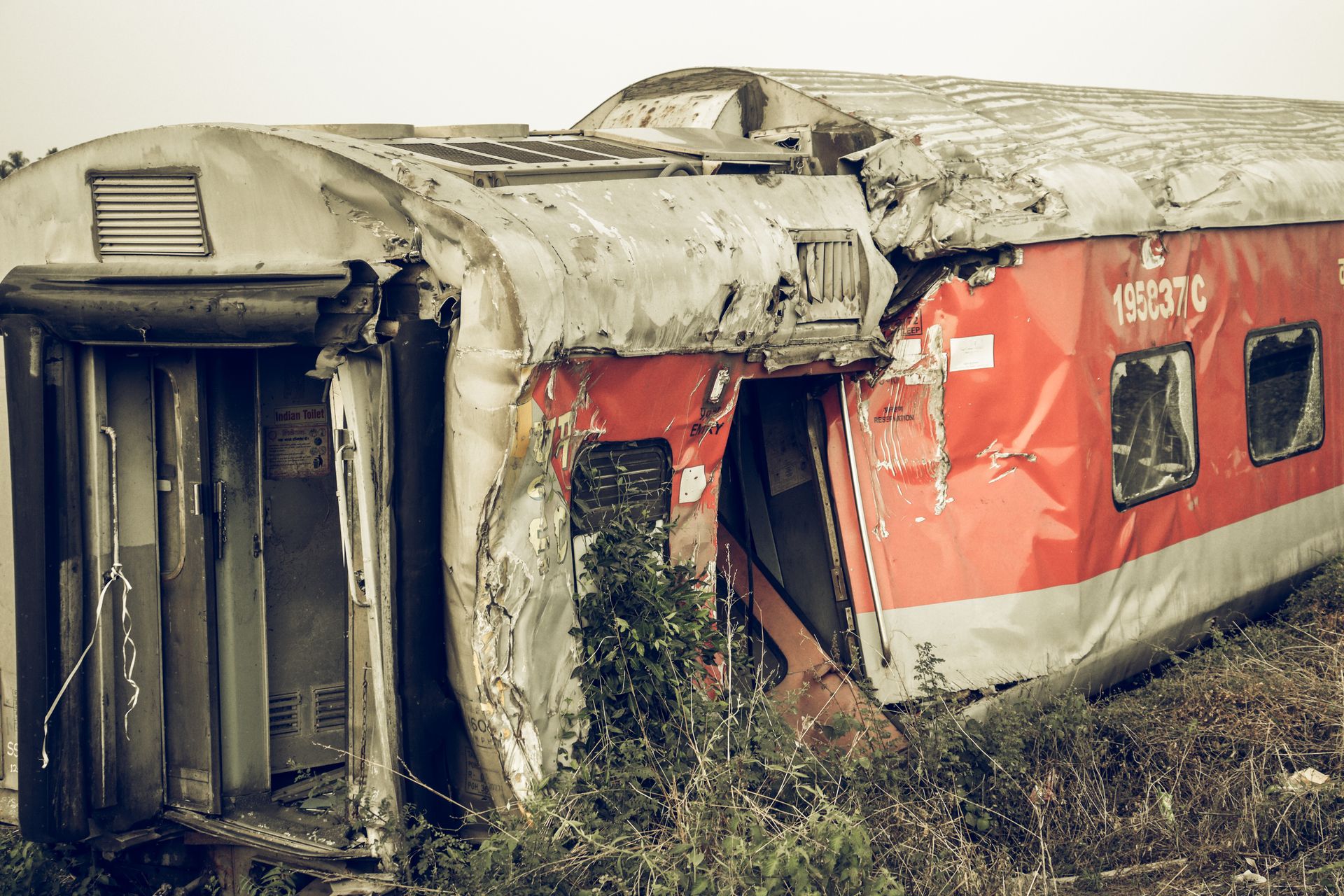 A dilapidated train carriage lying abandoned in an overgrown field after derailing.