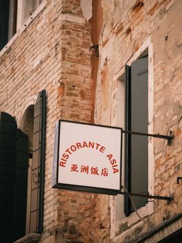 Discover a Venice street featuring the 'Ristorante Asia' sign on a rustic brick building facade.