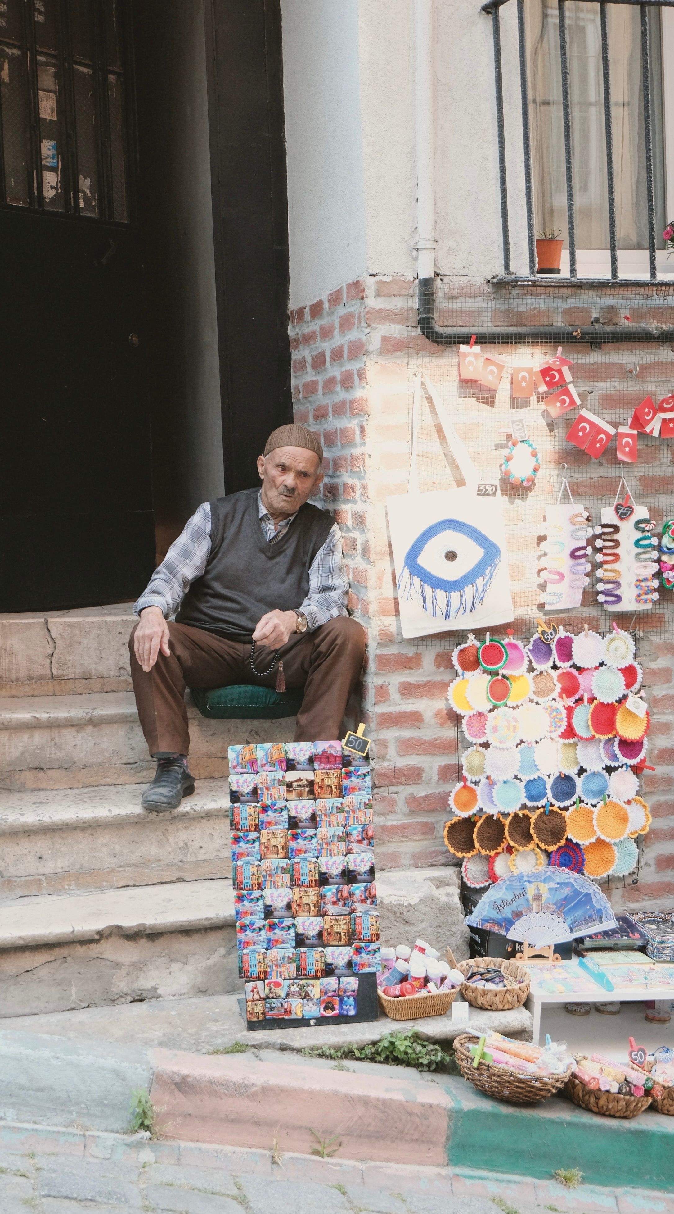 A street vendor sits by colorful handmade crafts and souvenirs in a quaint setting.