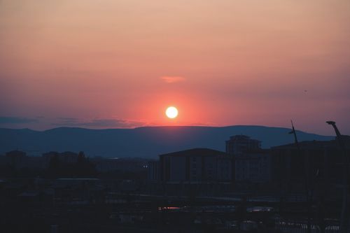 Free A stunning sunset casting vibrant colors over the silhouette of an urban cityscape. Stock Photo