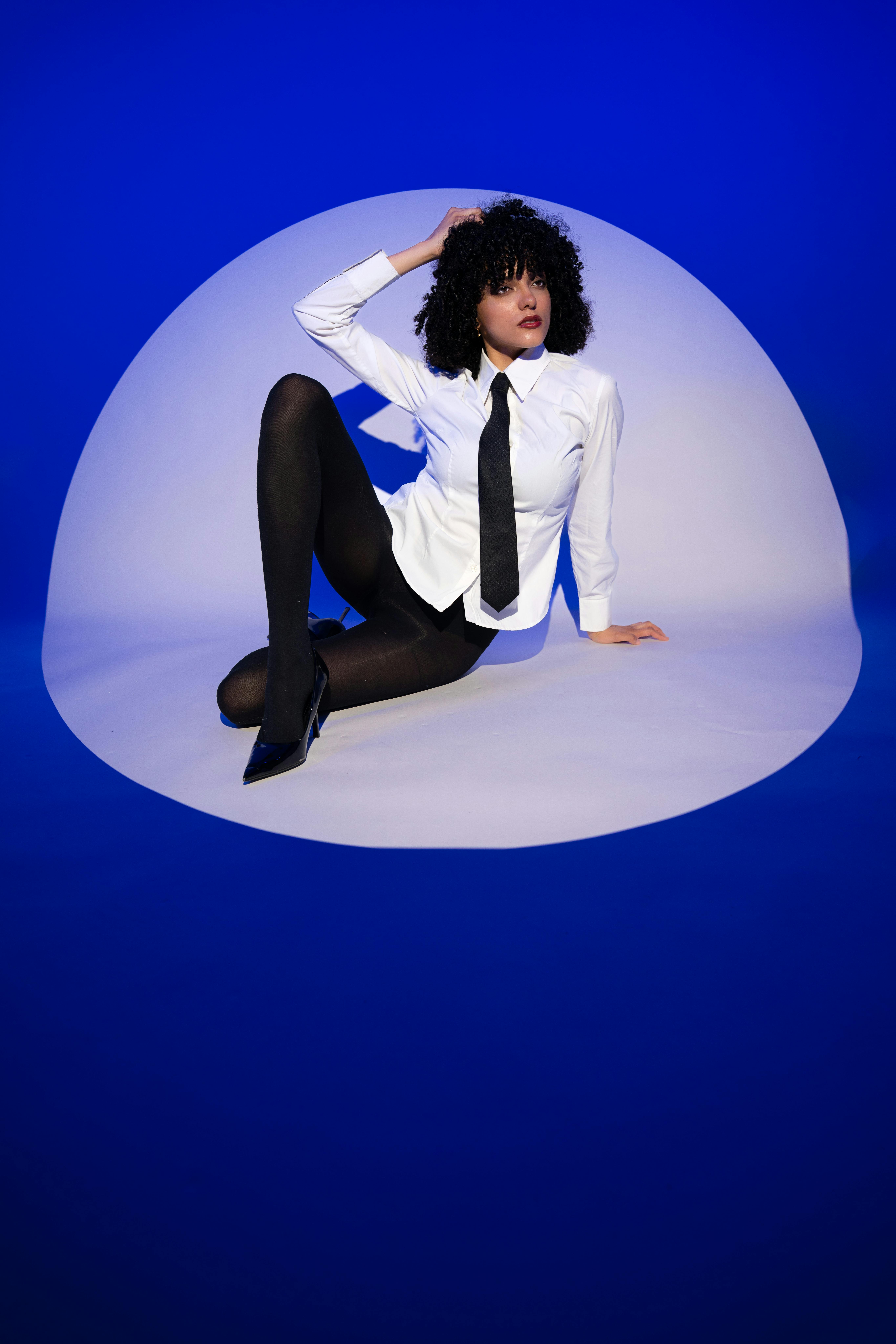 Zadarmo Umelecký portrét ženy sediacej s modernou pózou v modrom štúdiovom prostredí. Fotka z fotobanky