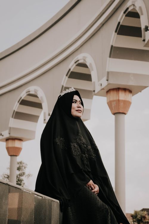 Free A woman in a black hijab sits gracefully against an architectural backdrop. Stock Photo