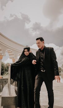 一对身着优雅黑色服装的情侣，在多云的天空下并肩散步