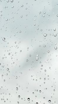 Close-up of raindrops on a window with overcast sky in the background, emphasizing weather elements.