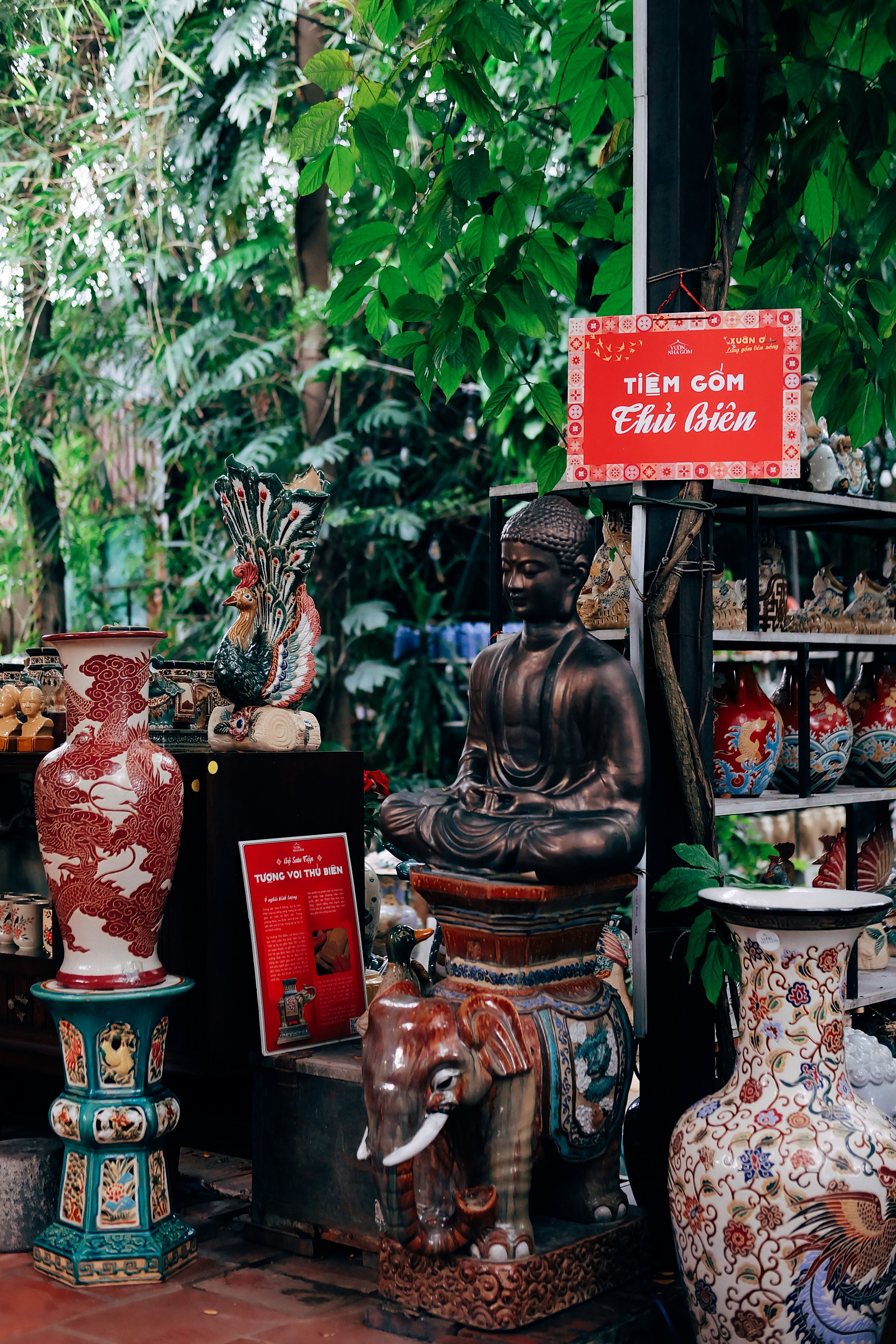 Outdoor display of Asian pottery and Buddha statue amidst lush greenery.
