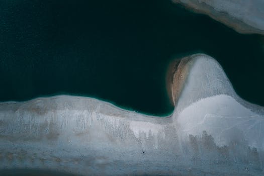 Aerial shot showcasing a serene ocean shoreline with clear water and sandy beach.