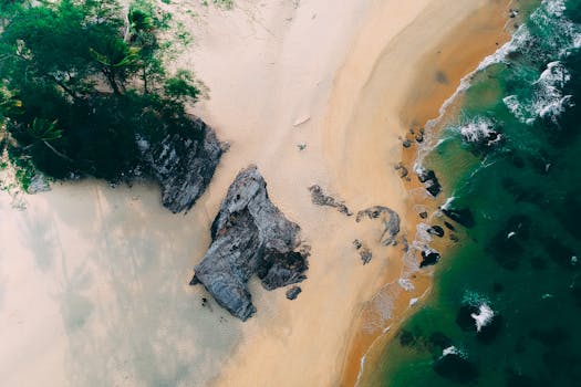 Breathtaking aerial view of a sandy beach meeting rugged rocks and vibrant ocean waves.