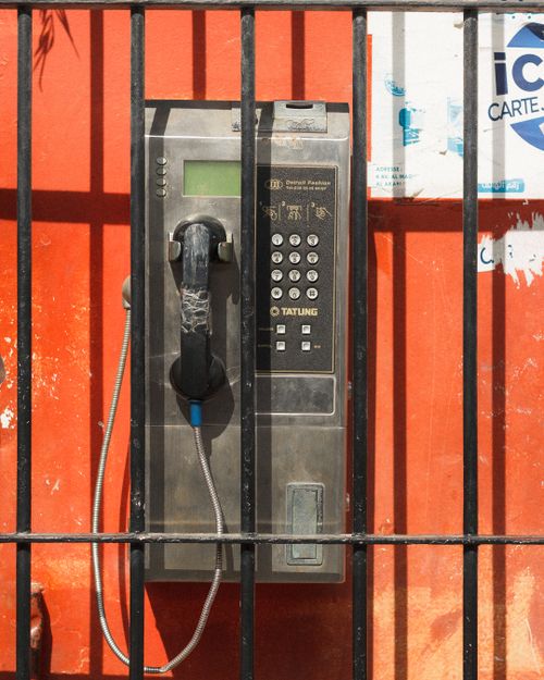 Free Old-style payphone against a bright orange wall behind black bars outdoors. Stock Photo