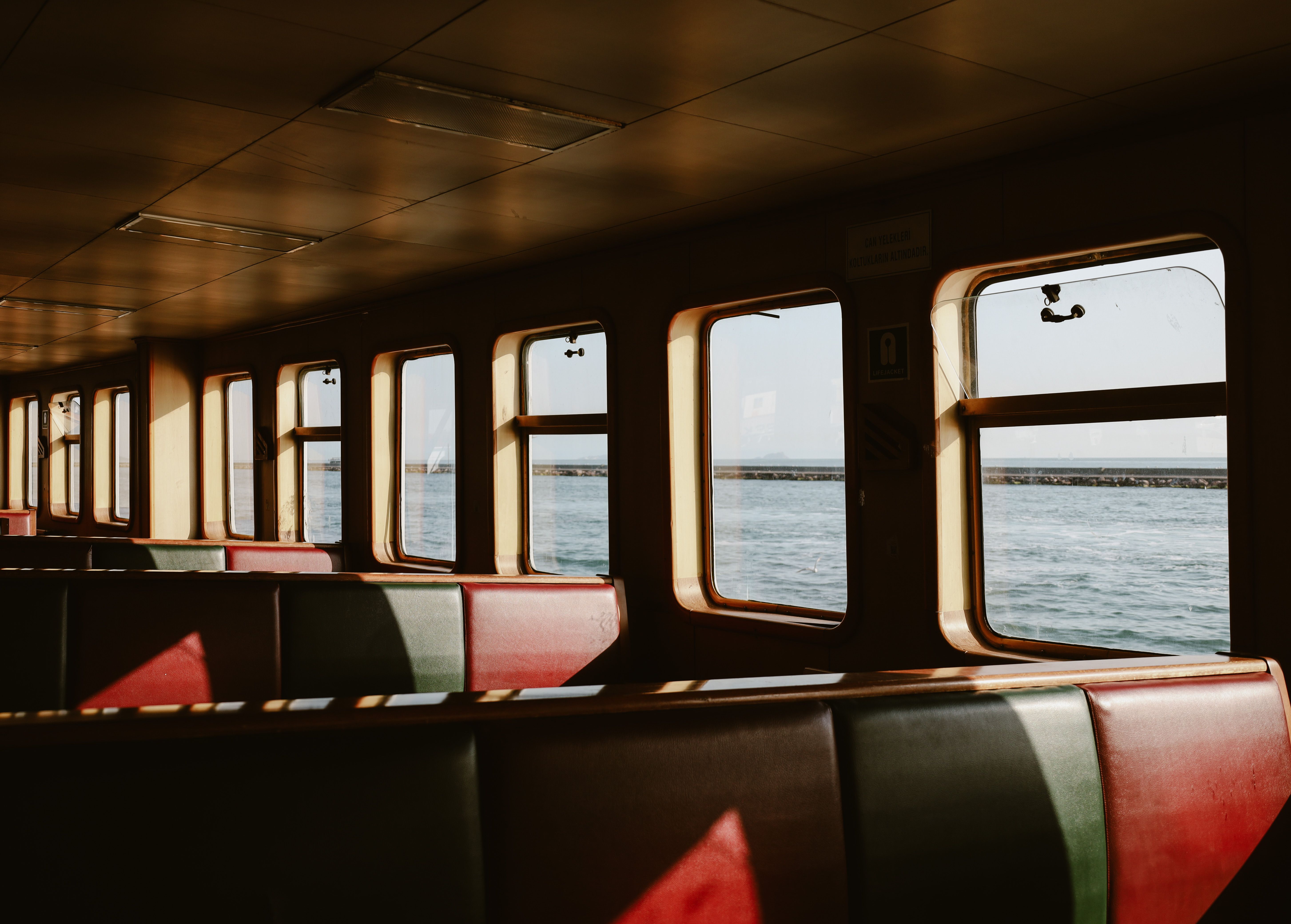Interior of an Istanbul ferry with empty seats and a view of the sea through windows at sunset.