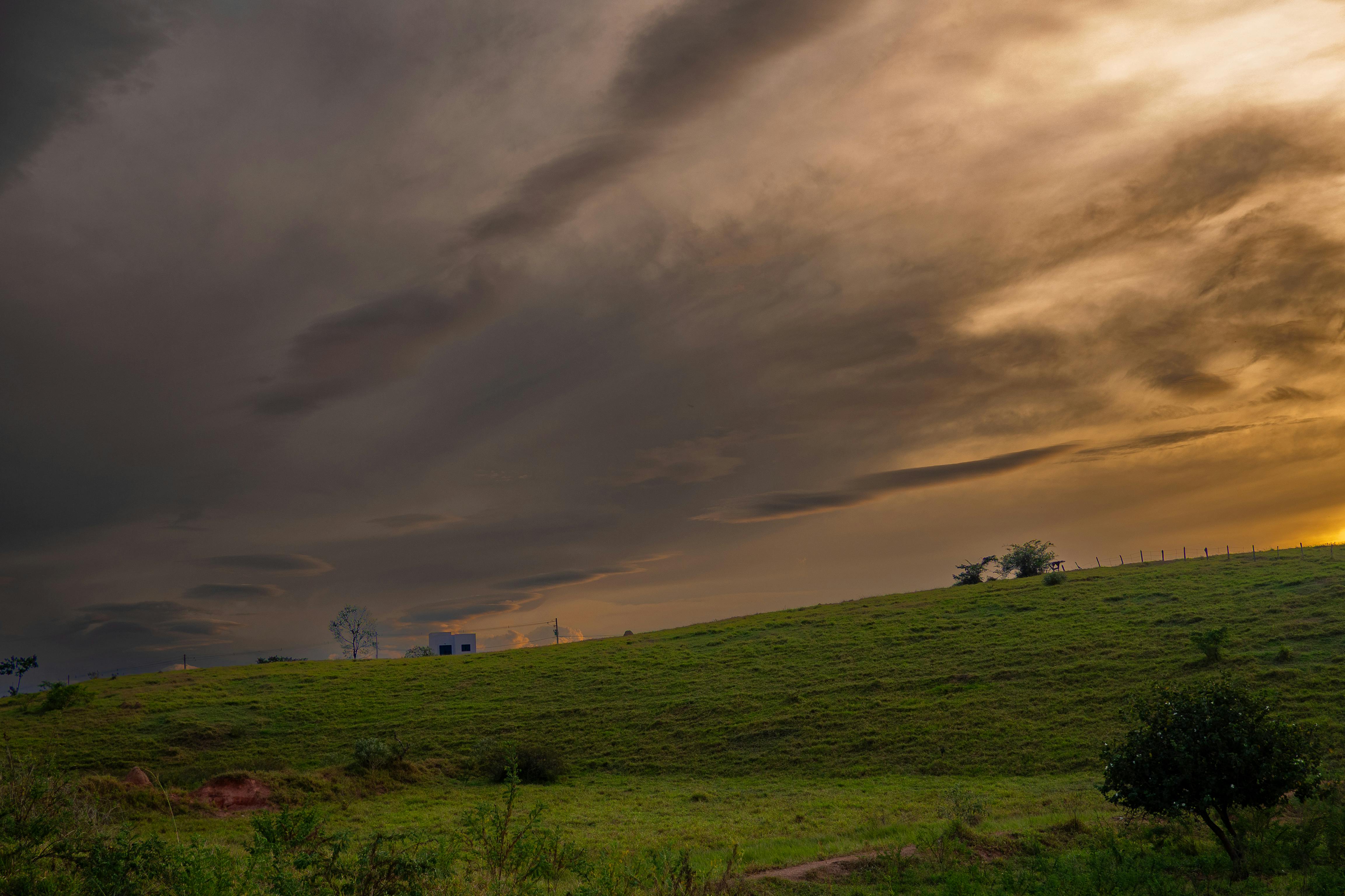 Sunset view over green hills with dramatic cloudy sky, serene and peaceful scene.