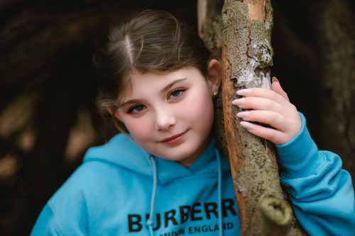 Free Close-up portrait of a girl leaning on a tree outdoors in a blue hoodie. Stock Photo