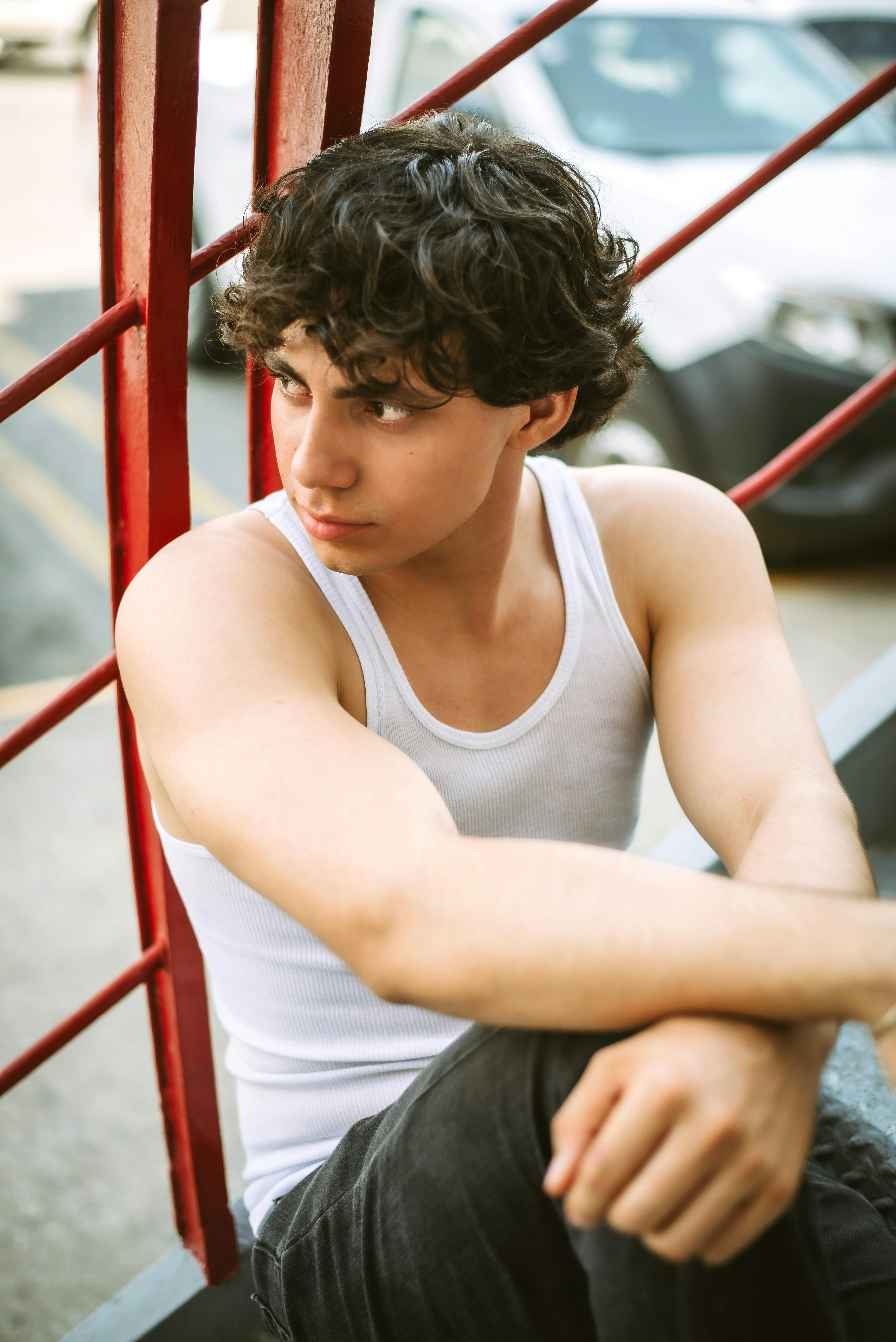 Casual portrait of a young man in a white tank top sitting outdoors.
