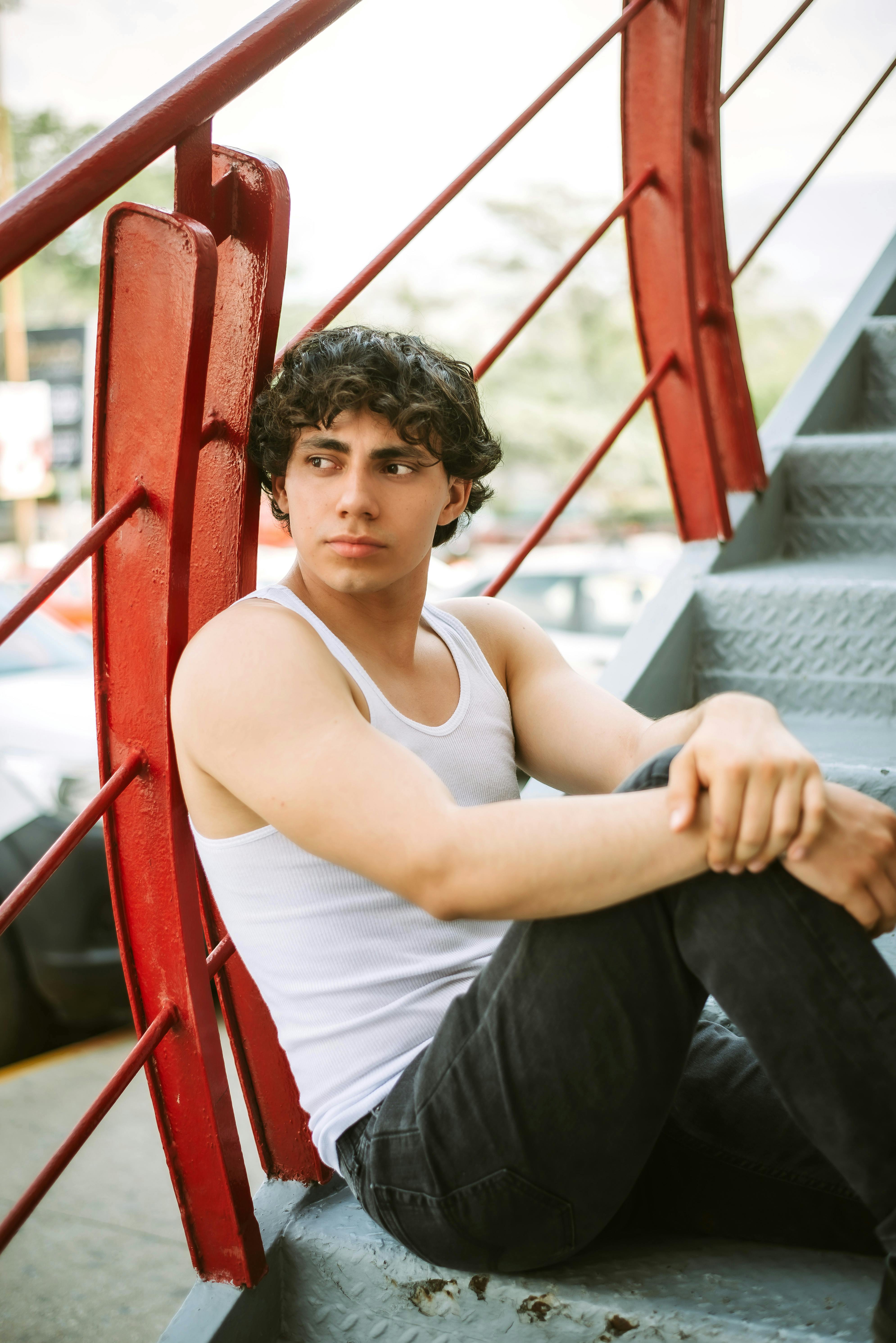 Young man in casual attire sits on outdoor stairs, gazing thoughtfully.