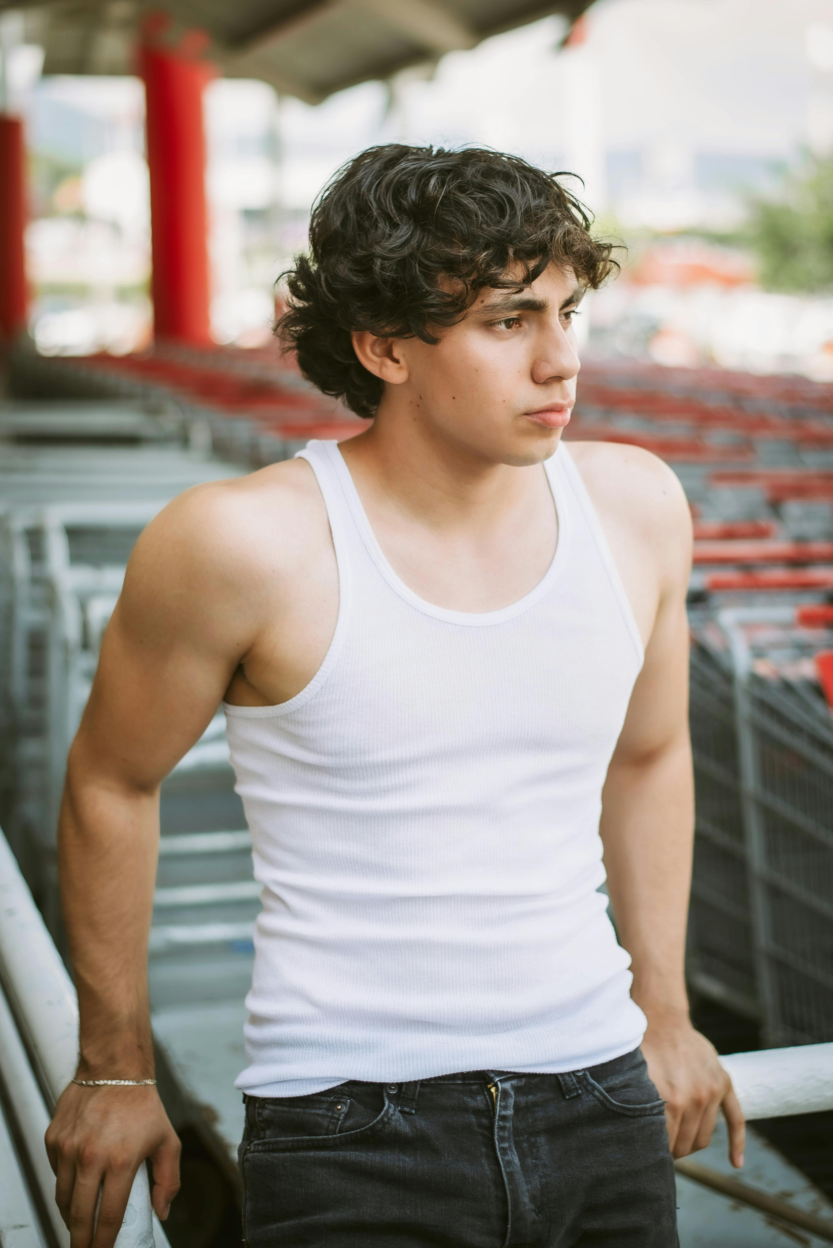 Portrait of a young man in a white tank top leaning casually in an urban environment.