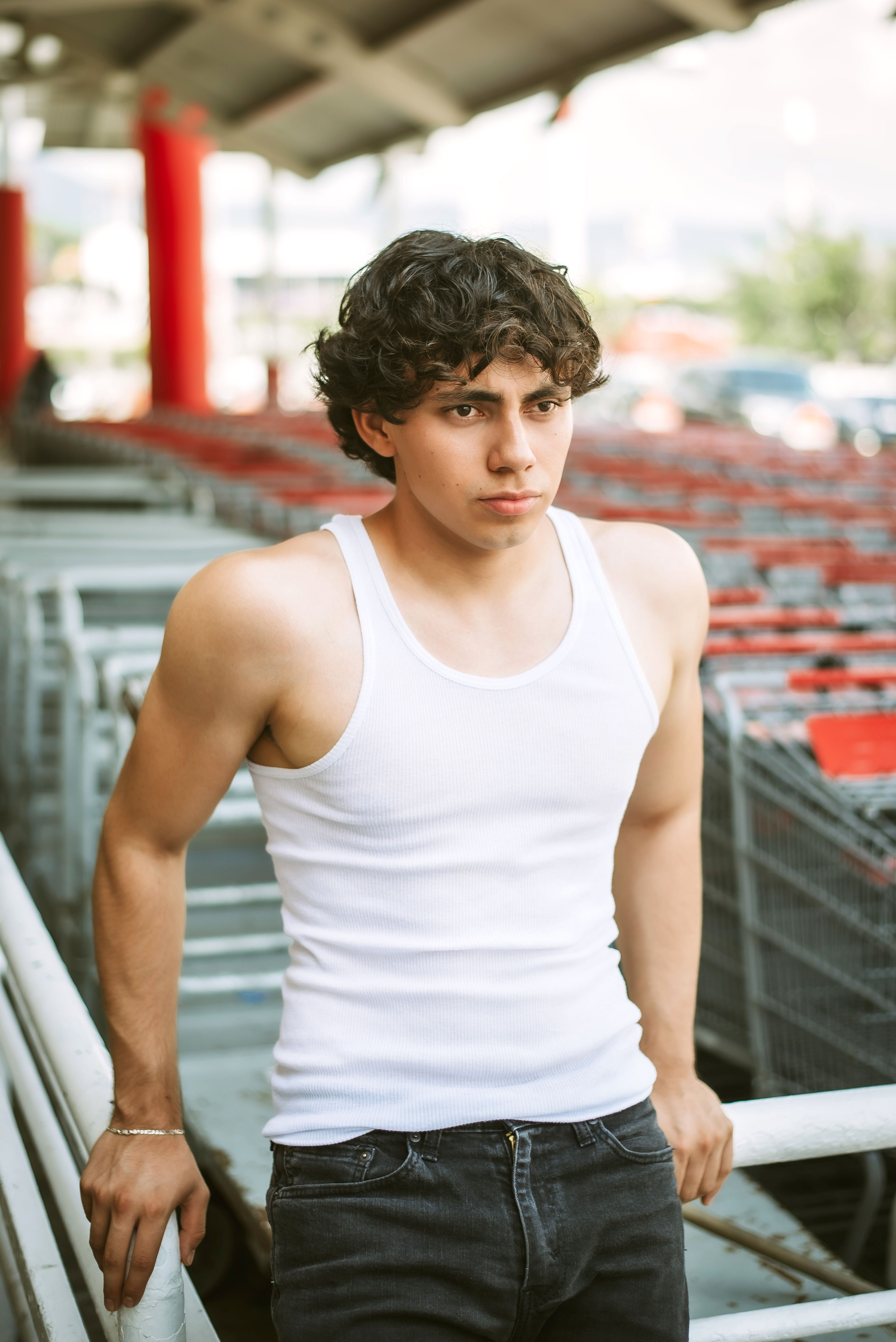 Young man in a white tank top leaning on shopping carts outdoors