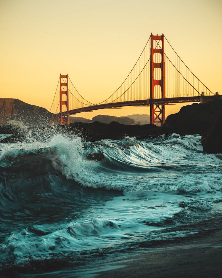 Low Angle Shot Of Strong Waves Crashing On The Shores Under Golden Gate Bridge