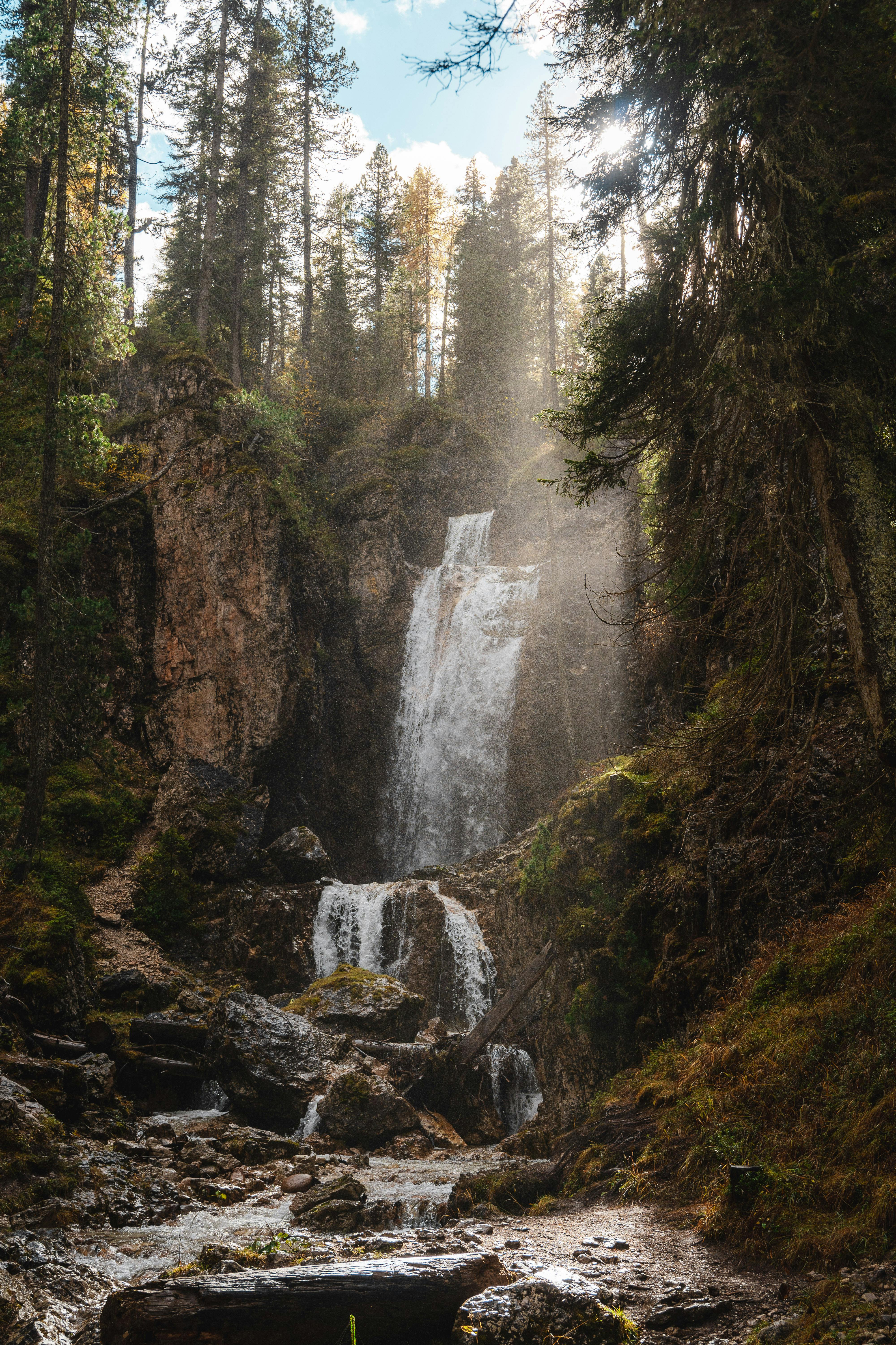 Beautiful waterfall cascading in a serene forest setting, surrounded by tall trees and sunlight.