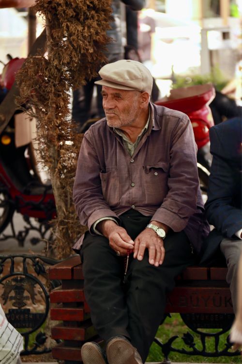 Free An elderly man wearing a cap sits on a park bench, enjoying a peaceful moment outdoors. Stock Photo