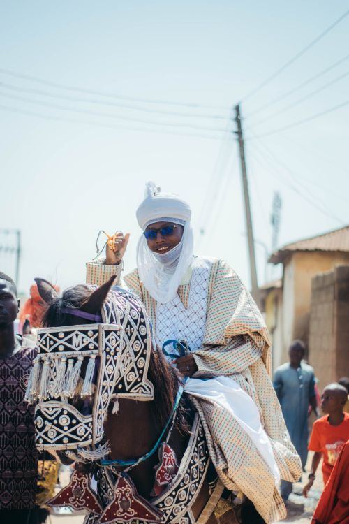Free Man in traditional attire rides decorated horse in vibrant African street parade. Stock Photo