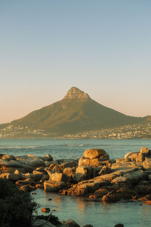 Free Scenic view of Lion's Head mountain from a rocky beach in Cape Town at sunset. Stock Photo