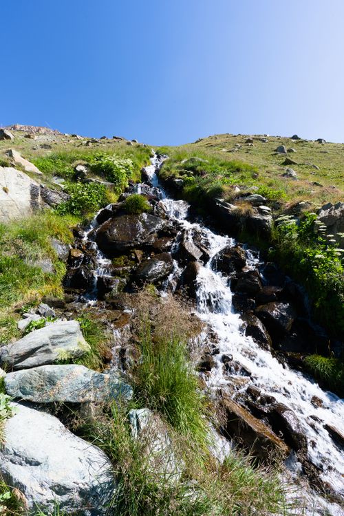 Free Serene mountain waterfall cascading down rocks in Zermatt, Switzerland, under a clear blue sky. Stock Photo