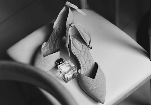 Black and white image of stylish shoes and perfume bottle on chair.
