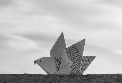 Free Minimalist black and white photo of an origami bird against a cloudy sky, symbolizing peace and creativity. Stock Photo