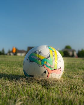 A colorful soccer ball resting on a green field under clear blue skies.