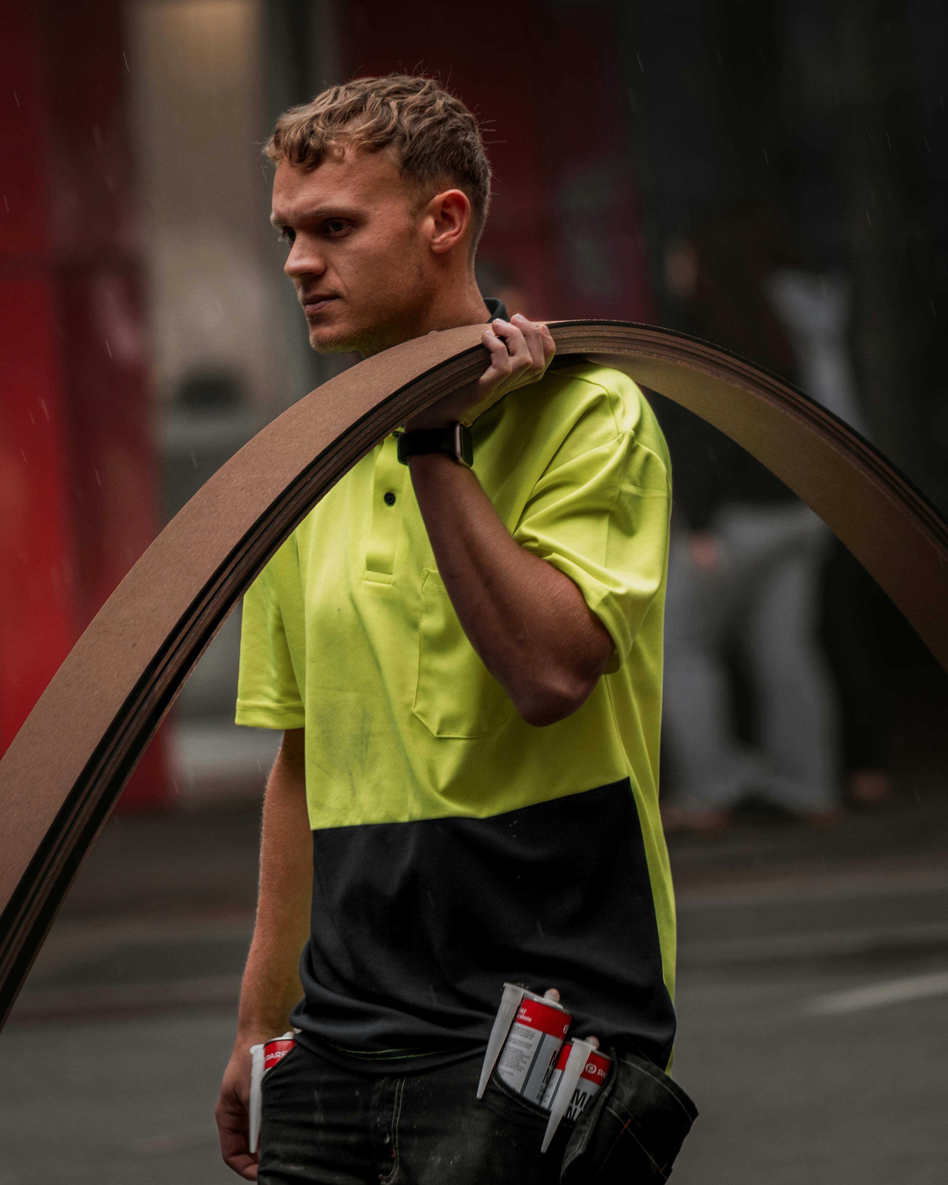 Gratuit Un muncitor în construcții, îmbrăcat într-o vestă de siguranță neon, care transportă materiale pe o stradă din Perth. Fotografie de stoc