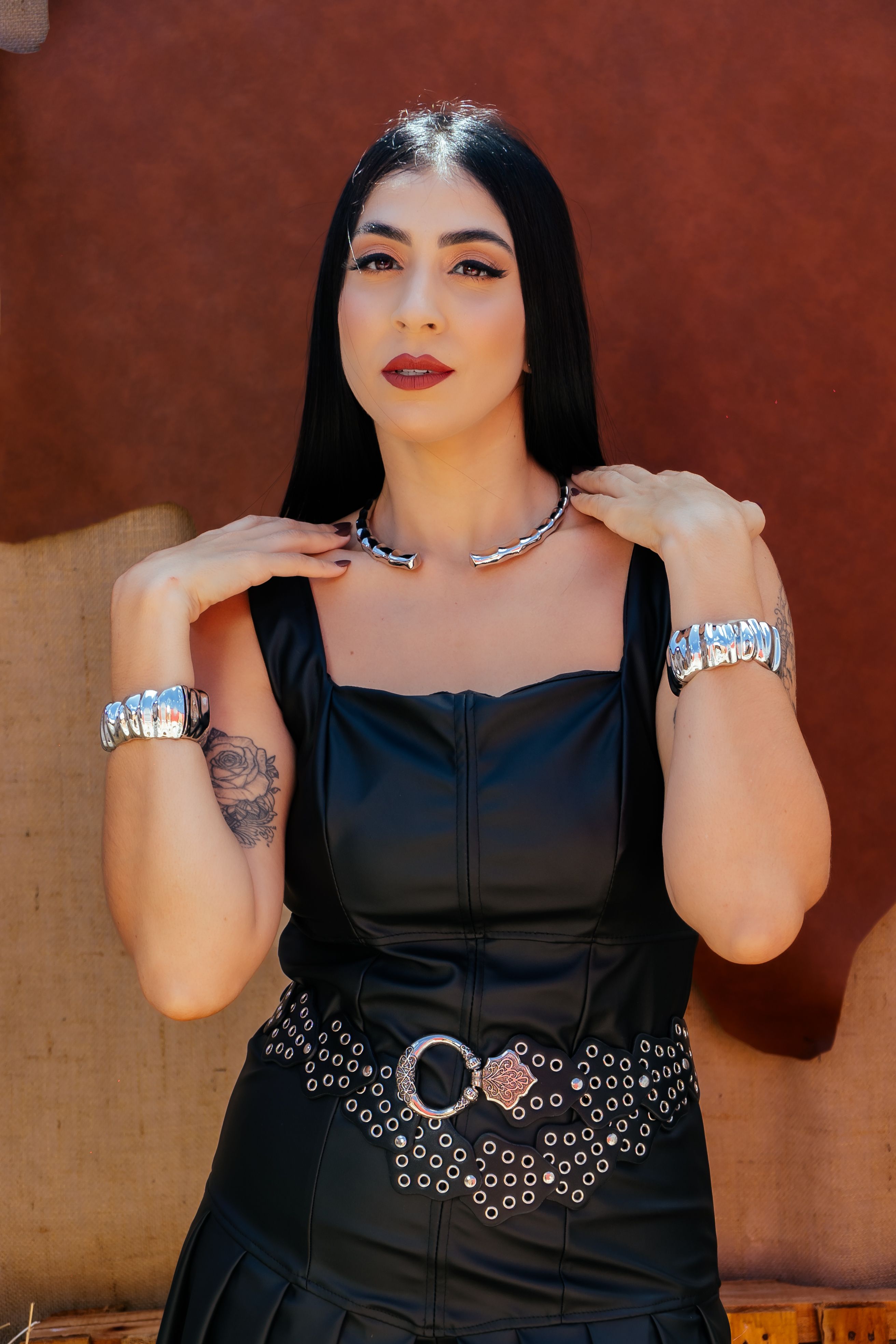 Mulher usando vestido de couro preto com joias de prata posa confiante ao ar livre.