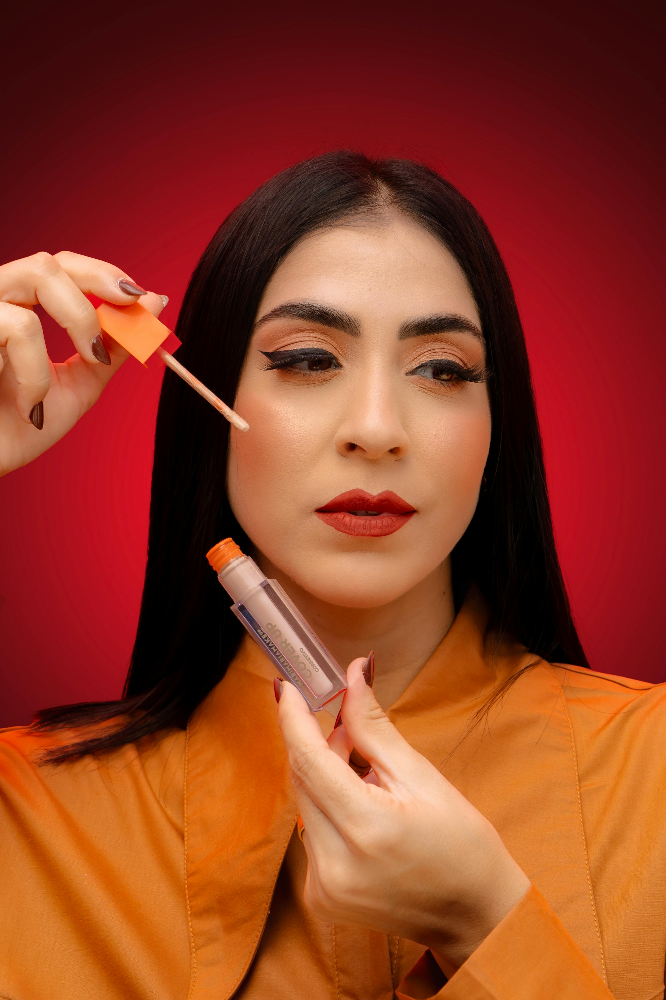 Portrait of a woman applying lip gloss with a red background highlighting her beauty.