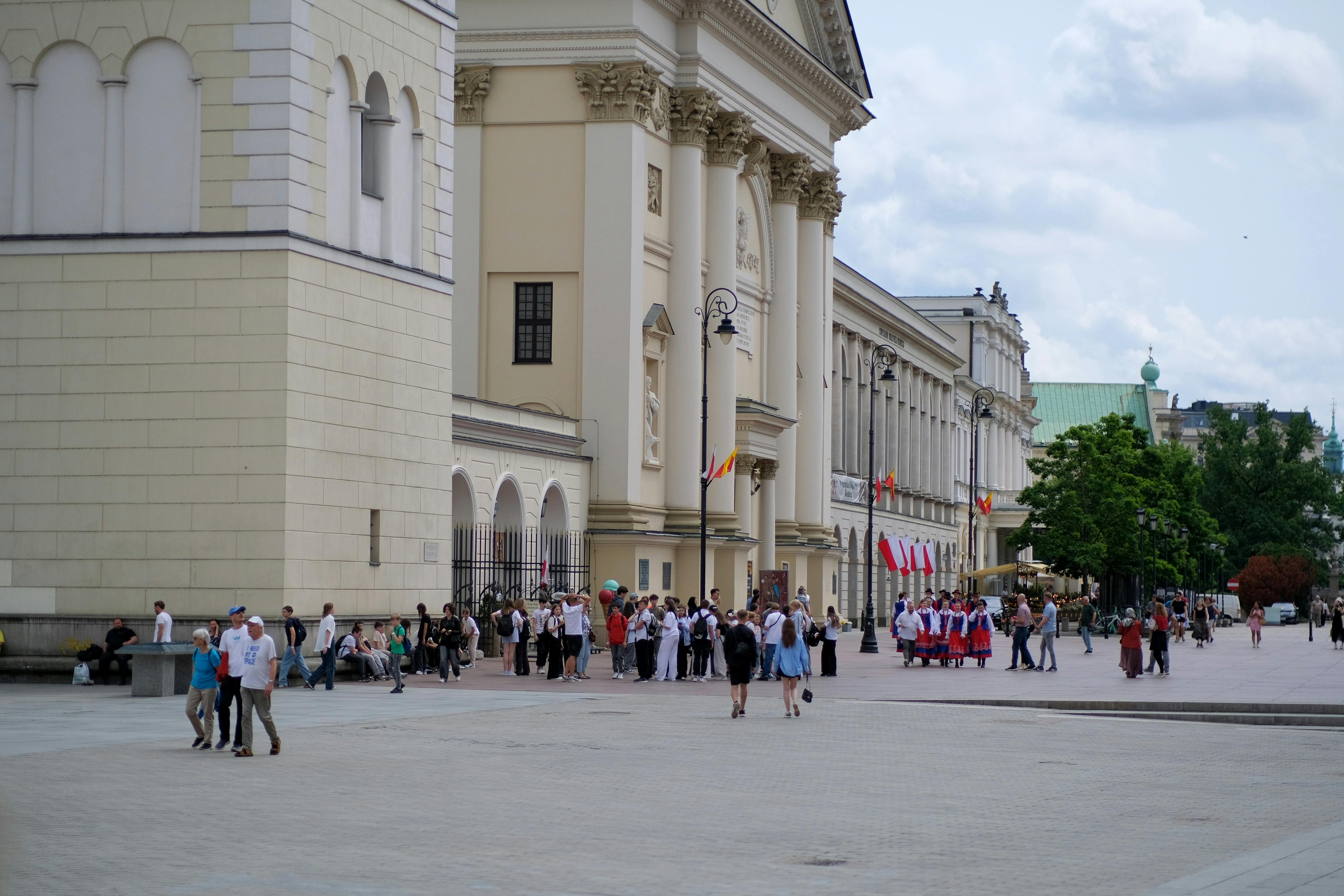Bezpłatne Ludzie zbierają się w pobliżu zabytkowego budynku, gdzie w pogodny dzień tętnią życiem liczne atrakcje, a powiewają flagi. Zdjęcie z galerii