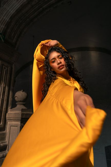 Dynamic portrait of a model in a flowing yellow dress with dramatic light and shadow interplay in an architectural setting.